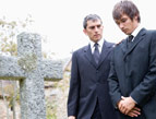 men mourning at a graveyard near a cross