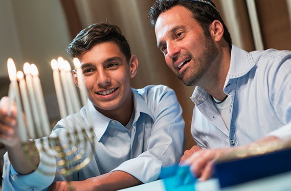 A son lights the Menorah together with his father to celebrate Hannukah.
